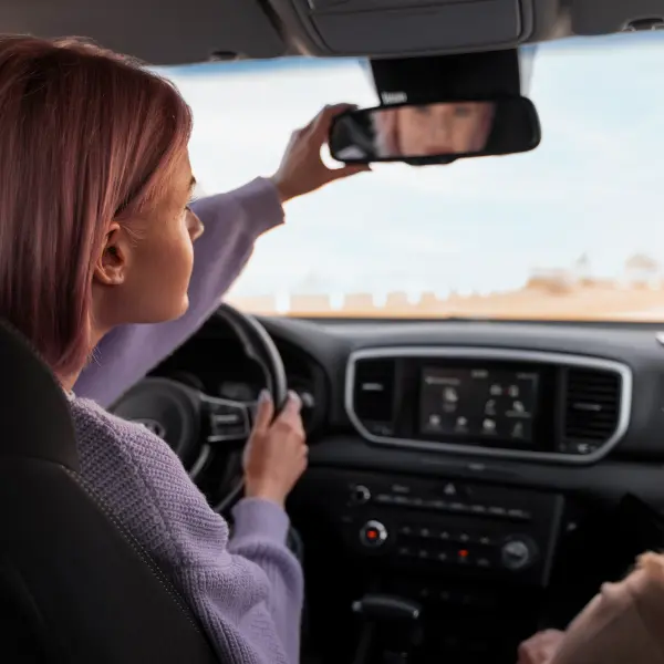 Une jeune femme blonde au volant d'une voiture réajustant son rétroviseur intérieur