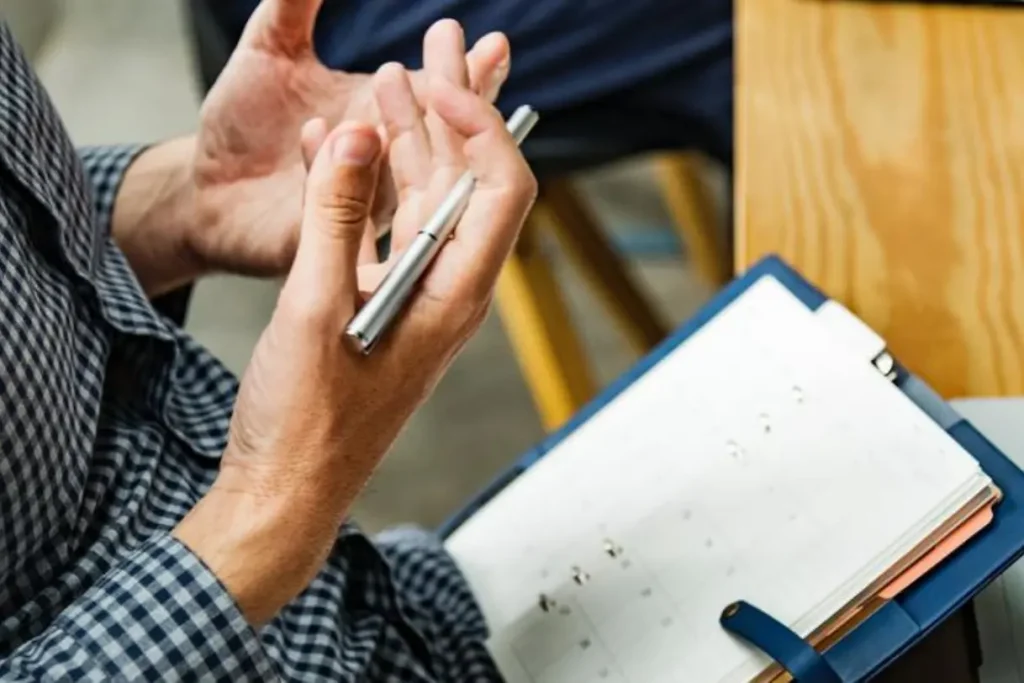 Inspecteur tenant un stylo dans sa main droite et un carnet de documents sur ses genoux, expliquant quelque chose à quelqu'un.