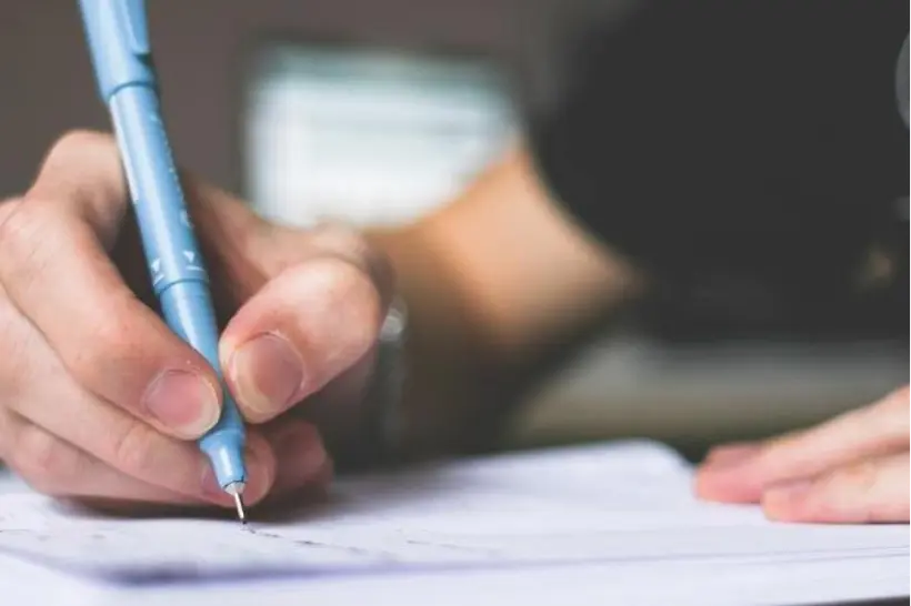 Personne écrivant sur une feuille de papier, installé sur un bureau.