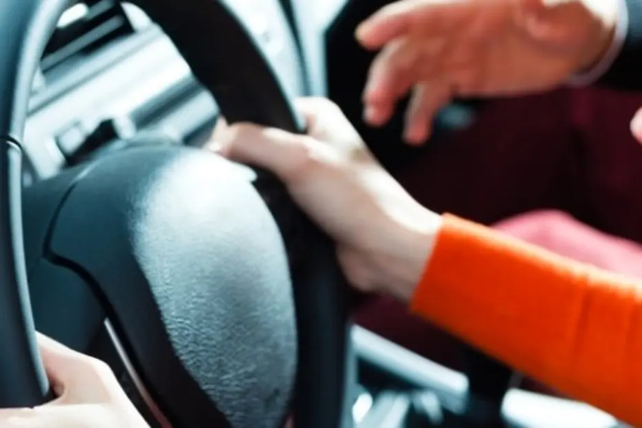 Plan sur les mains d'un conducteur tenant un volant, accompagné d'un inspecteur sur le siège passager dans une voiture.