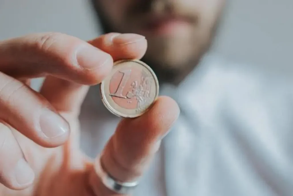 Homme habillé d'une chemise, tenant une pièce d'un euro côté pile, proche de la caméra